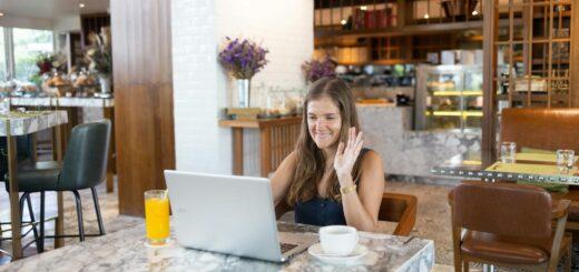 Woman smiling and waving during video call at a chic cafe with a marble table.
